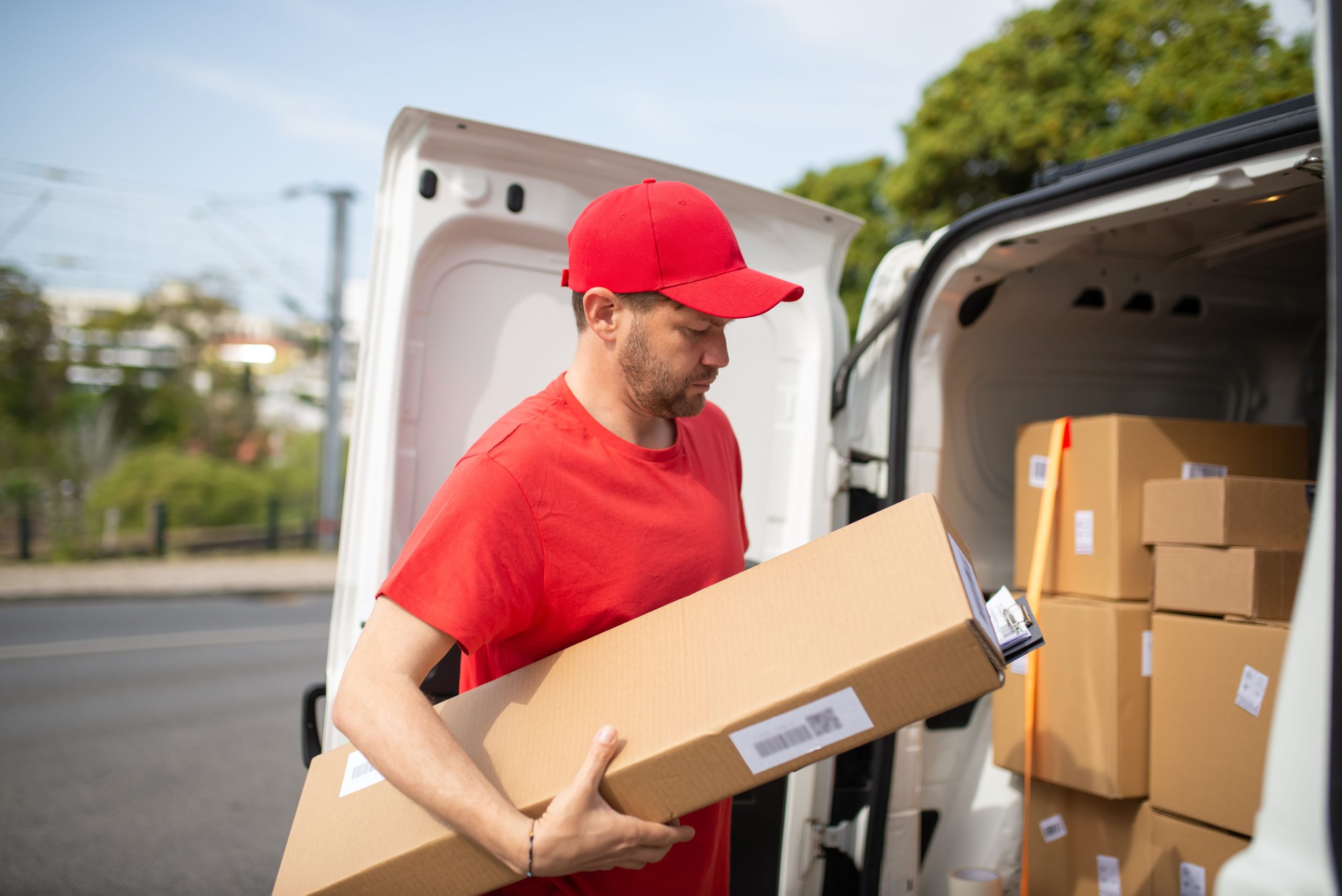 Courier in red uniform unloading packages from a delivery van on a sunny day.