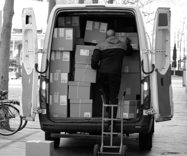 Monochrome image of a man loading packages into a van outdoors in the Netherlands.