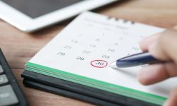 Close-up shot of a hand marking a date on a calendar with a pen, emphasizing planning and scheduling.