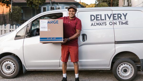 A courier in a maroon uniform smiling with a package in front of a delivery van.